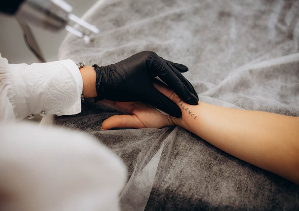 Beautician using laser device to remove an unwanted tattoo from female arm. Concept of erasing tattoos as an expensive procedure in a cosmetology clinic.